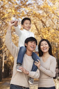 Boy sitting on his fathers shoulders in a park with family in Autumn