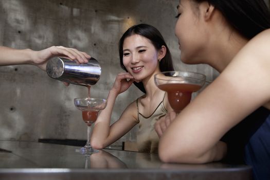 Young women having cocktails, sitting at the bar counter