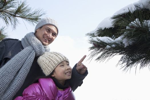Father with daughter pointing at tree branch covered in snow