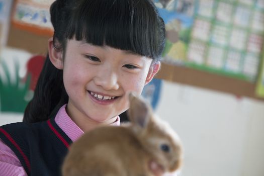 Schoolgirl holding pet rabbit in classroom