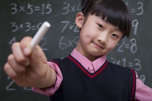 Portrait of schoolgirl in front of blackboard holding chalk 