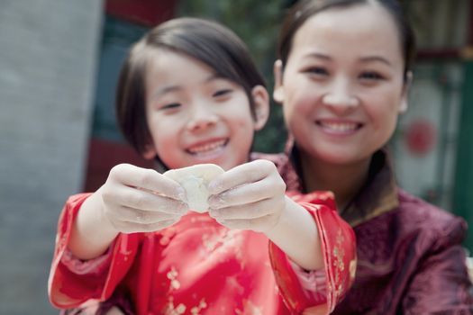 Mother and daughter making dumplings in traditional clothing, close up