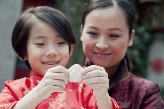 Mother and daughter making dumplings in traditional clothing, close up