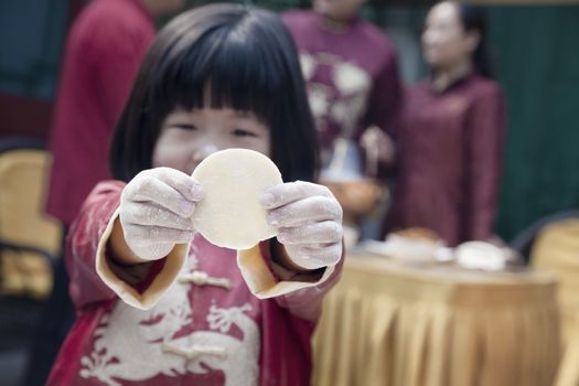 Little girl showing dumpling wrapper in traditional clothing