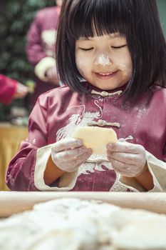 Portrait of little girl making dumplings in traditional clothing