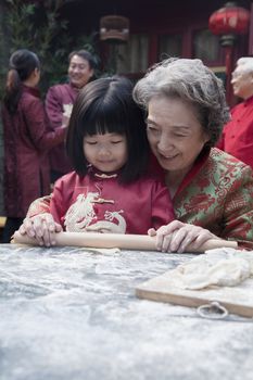 Grandmother and granddaughter making dumplings in traditional clothing