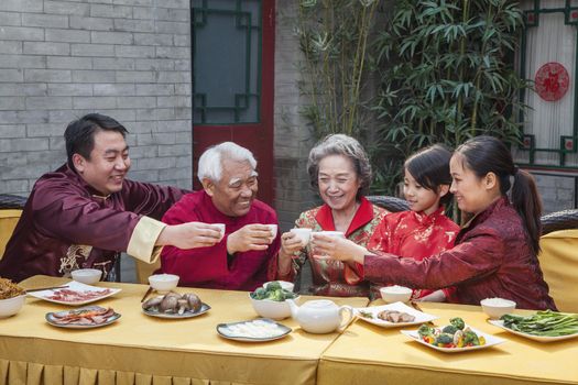 Family with cups raised toasting over a Chinese meal 