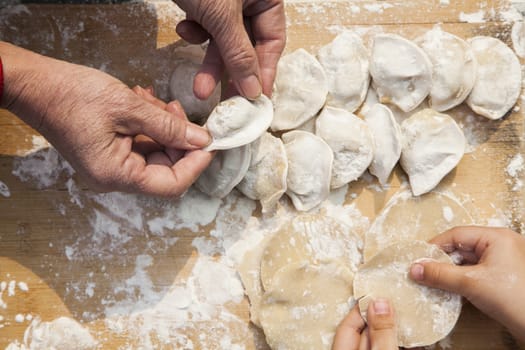 Senior woman and girl making dumplings, hands only