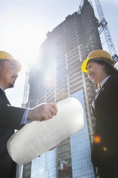 Two architects at a construction site holding blueprint