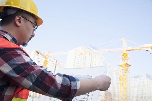 Architect looking at a blueprint outdoors at a construction site