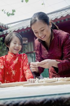 Mother and daughter making dumplings in traditional clothing