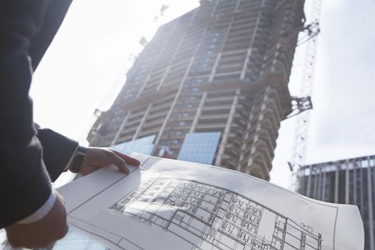 Architect holding blueprint of building at a construction site, midsection