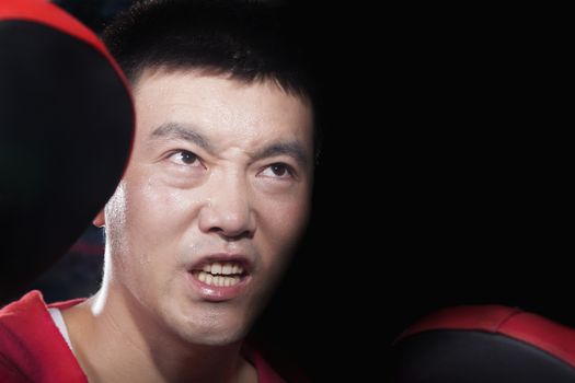 Portrait of aggressive looking boxing coach at the gym holding pads