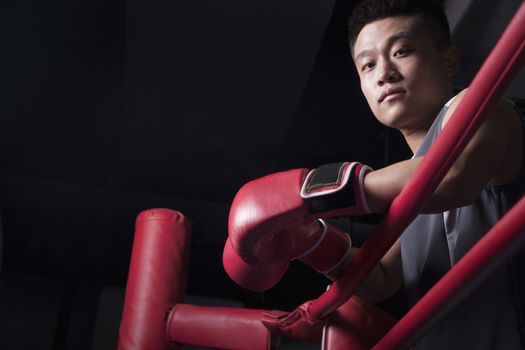 Portrait of male boxer resting his elbows on the ring side, looking at camera, low angle view