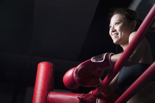 Smiling female boxer resting her elbows on the ring side, looking away, low angle view
