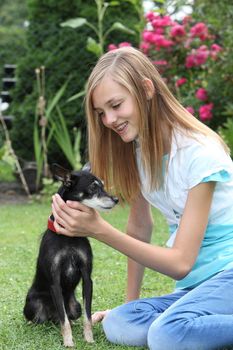 Affectionate young teenager caressing her loyal pet, a miniature pinscher dog, as the two enjoy the summer day sitting on the lawn