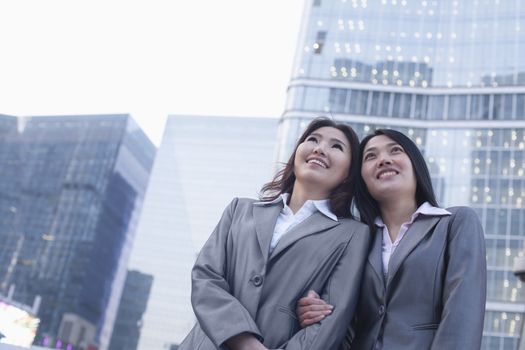 Portrait of smiling businesswomen linking arms, outdoors, Beijing  