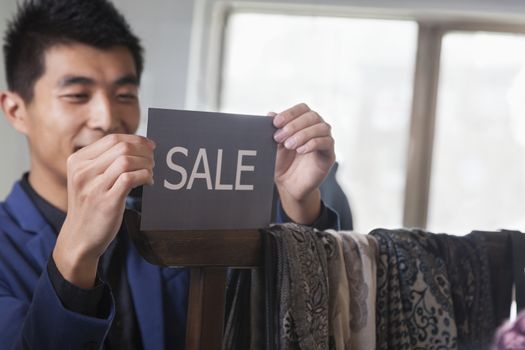 Store clerk putting up ""for sale"" sign at fashion store