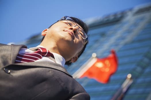 Low angle view of young businessman in front of a building with Chinese flag in the background