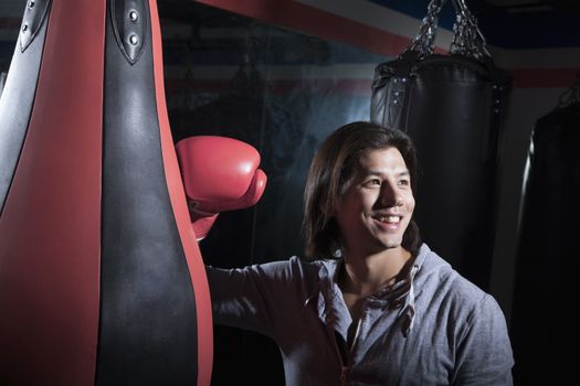 Portrait of smiling young man at the boxing gym leaning on punching bag