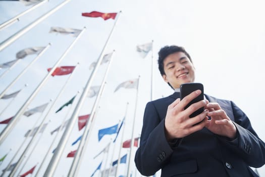 Smiling young businessman texting on his phone outdoors with flags in the background