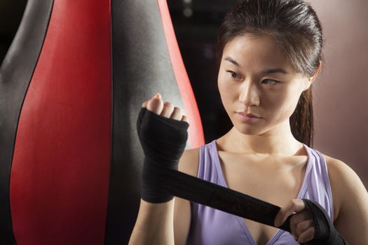 Young confident female boxer wrapper her wrists in the gym 