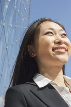 Young smiling businesswoman outside in front of glass building, close-up