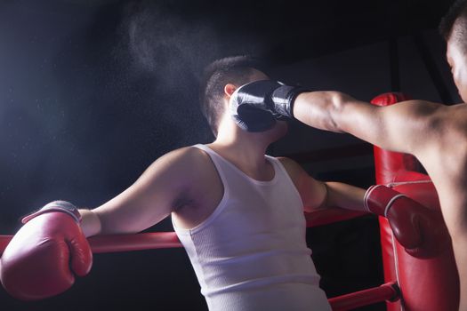 Over the shoulder view of male boxer throwing a knockout punch in the boxing ring