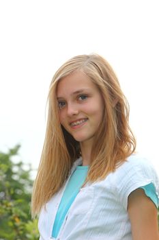 Attractive blond teenage girl with dental braces on her teeth smiling at the camera against a bright sky, low angle view