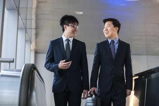 Two smiling businessmen coming up the escalator together