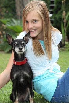 Proud little miniature pinscher dog sitting on the lawn with an alert look accompanied by its loving owner, an attractive young teenage girl