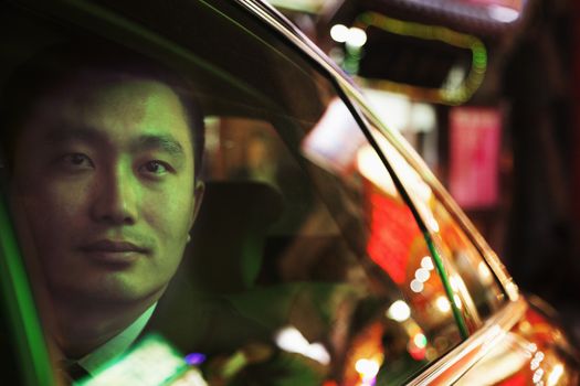 Contemplative Businessman in the back seat of a car looking out through window at night, Beijing