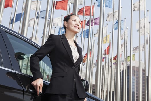 Businesswomen standing near car with flagpoles in background.