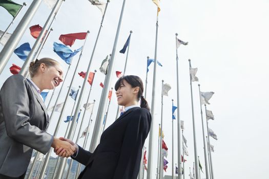 Two young businesswomen shaking hands outdoors  