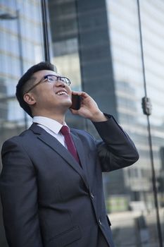 Smiling businessman on the phone outside in Beijing looking up
