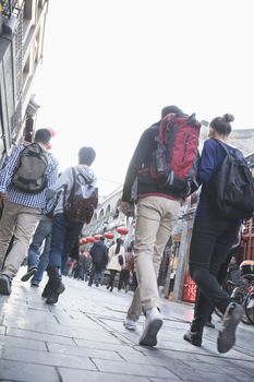 Group of young people walking down busy street, rear view.