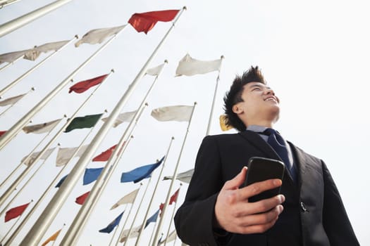 Smiling young businessman holding a phone with flags in the background