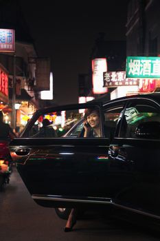 Businesswoman exiting car while on the phone, Beijing at nighttime