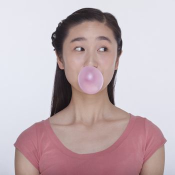 Young playful woman blowing a bubble out of  bubble gum, studio shot 