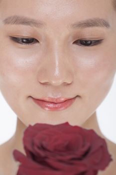 Close-up on the face of smiling beautiful woman looking down at a red rose, studio shot
