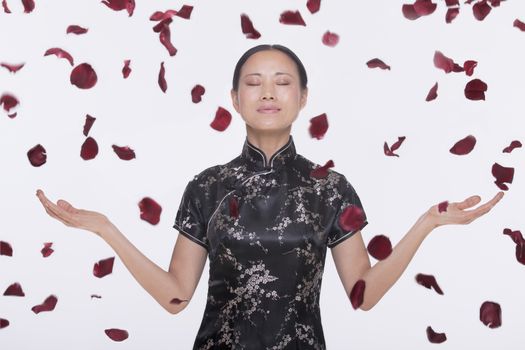 Woman in traditional clothing and arms outstretched with rose petals coming down around her in mid air, studio shot