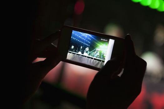 Young woman taking a photography with her smart phone at an indoor concert, Close-up on hands