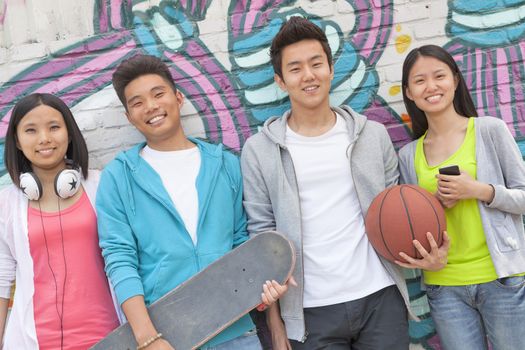 Portrait of four friends holding a skateboard and soccer ball hanging out in front of a wall covered in graffiti