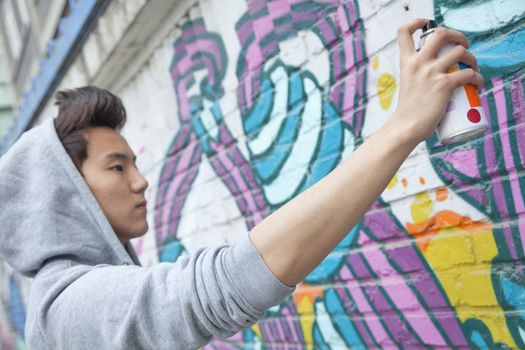 Serious young man concentrating while holding a spray can and spray painting on a wall outdoors