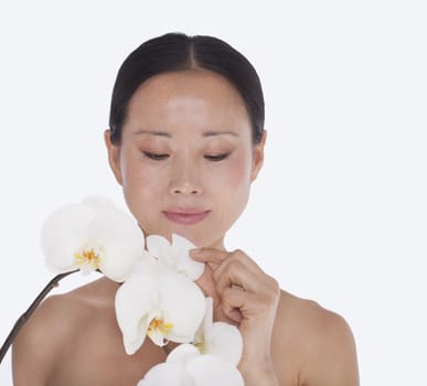 Serene shirtless woman looking down and touching a bunch of beautiful white flowers, studio shot