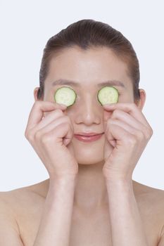 Smiling young shirtless woman holding cucumber slices over her eyes for a beauty treatment, studio shot