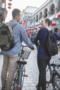 Young man and woman with bicycles, walking down street.