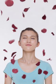 Beautiful tranquil young woman looking up with eyes closed with rose petals flying around her