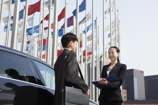 Two businesspeople meeting outdoors with flagpoles in background.