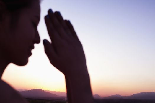 Serene young woman with eyes closed and hands together in prayer pose in the desert in China, focus on background